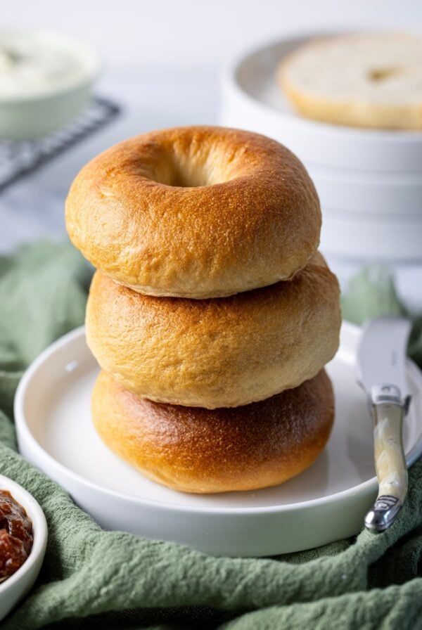 A stack of 3 golden brown sourdough bagels sitting on a white plate.