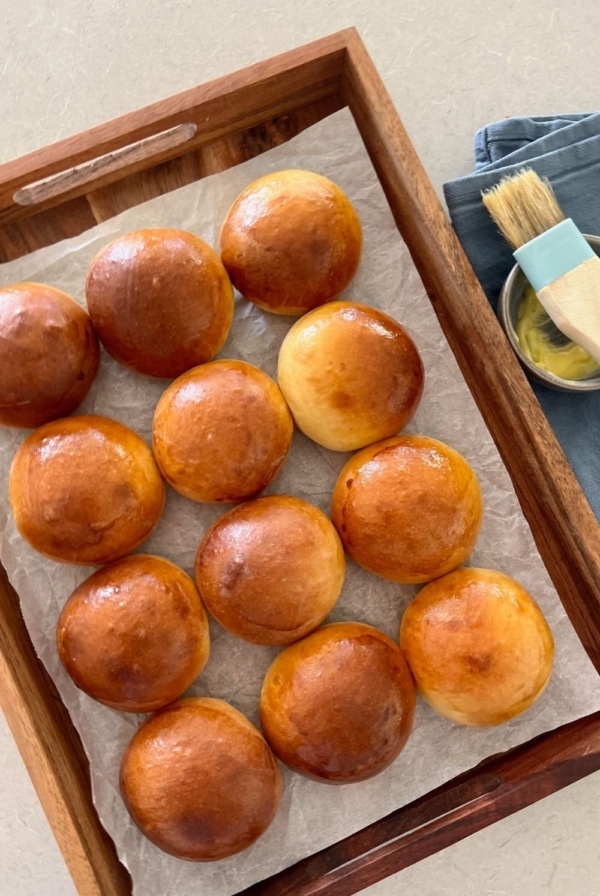Sourdough brioche buns displayed on a tray next to a pastry brush.