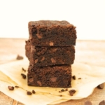 A stack of 3 sourdough brownies showing the crispy top and fudgy inside. There are some sourdough brownie crumbs around the stack.