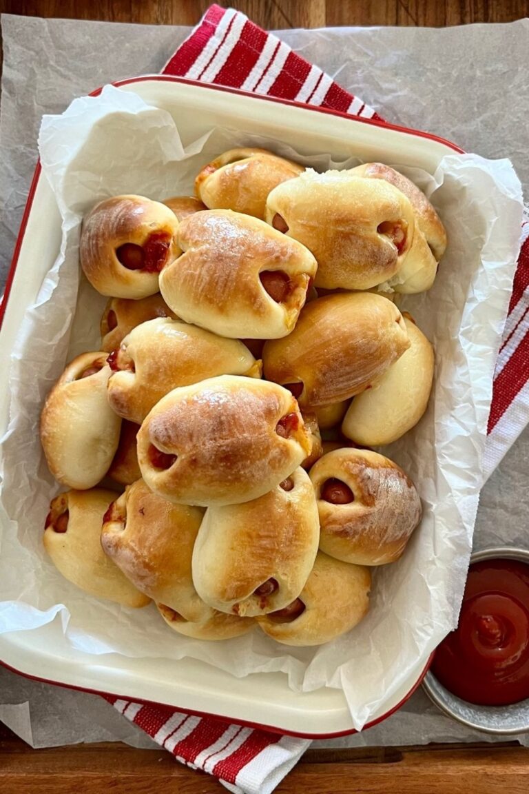 Sourdough pigs in blankets sitting in an enamel dish next to a plate of tomato ketchup