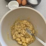 A bowl showing bananas being mashed with the back of a fork.