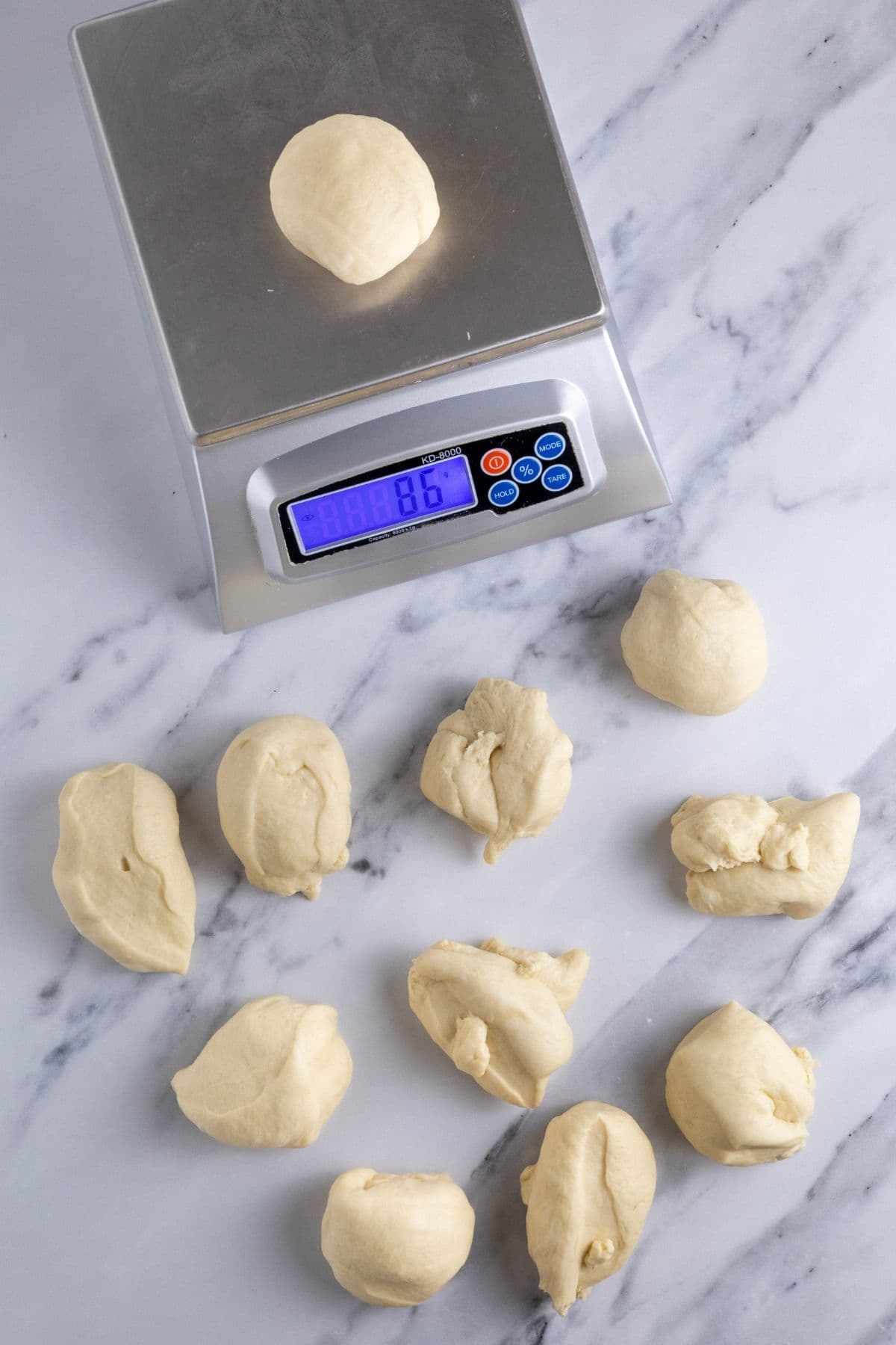 A photo showing 11 pieces of dough that have been weighed on a digital scale to exactly 86g each.