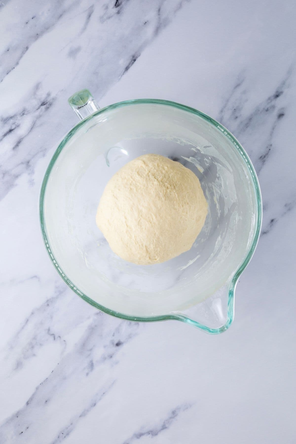 A glass bowl from a stand mixer with dough that has been kneaded into a smooth round ball.