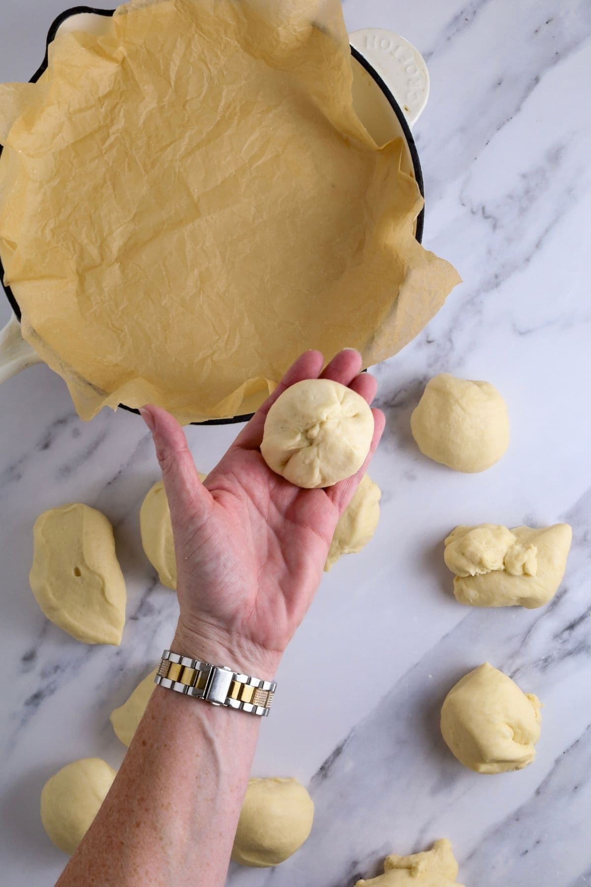 A hand holding a dough ball that has been shaped - you can see that the dough has been pulled together into the centre to form a ball.