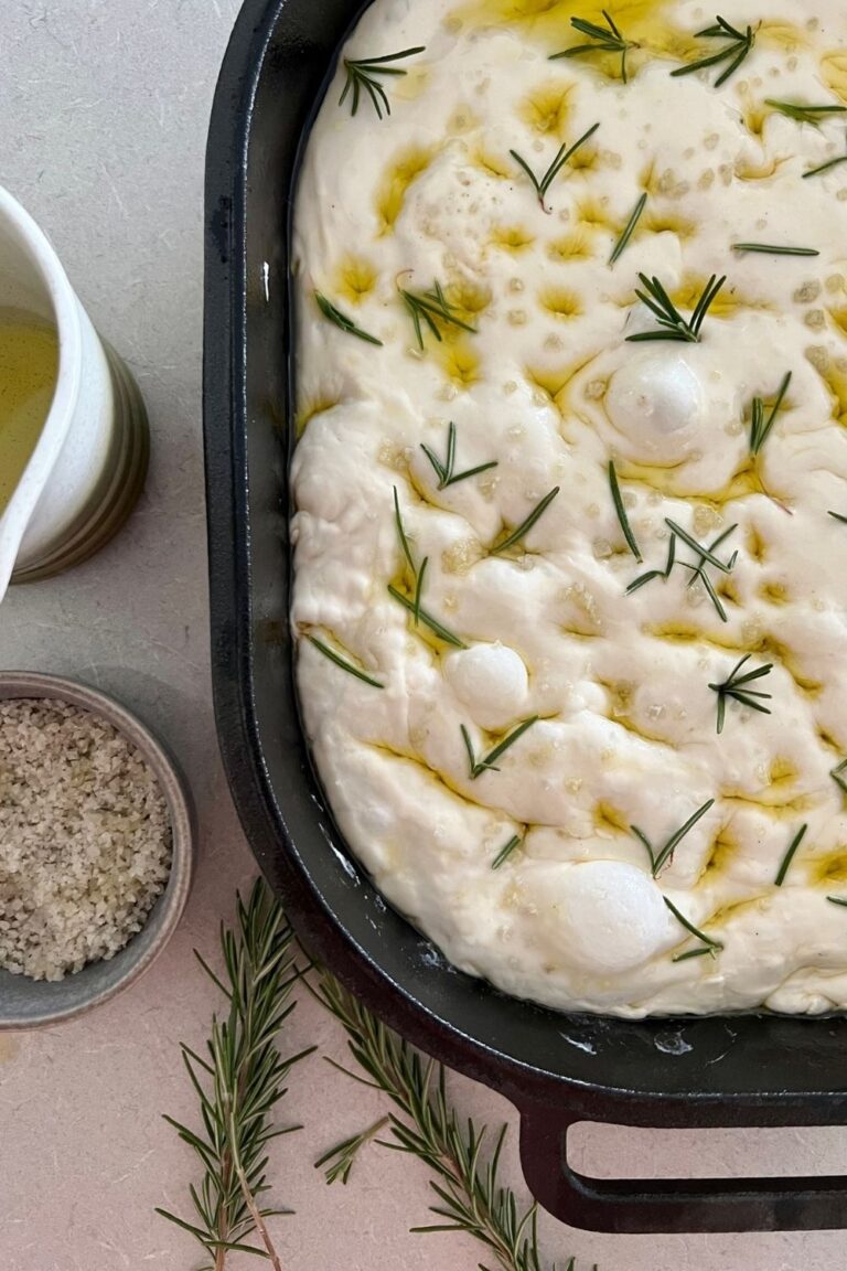 Sourdough focaccia bread recipe - bubbly sourdough focaccia in a black cast iron pan, studded with rosemary and drizzled with olive oil