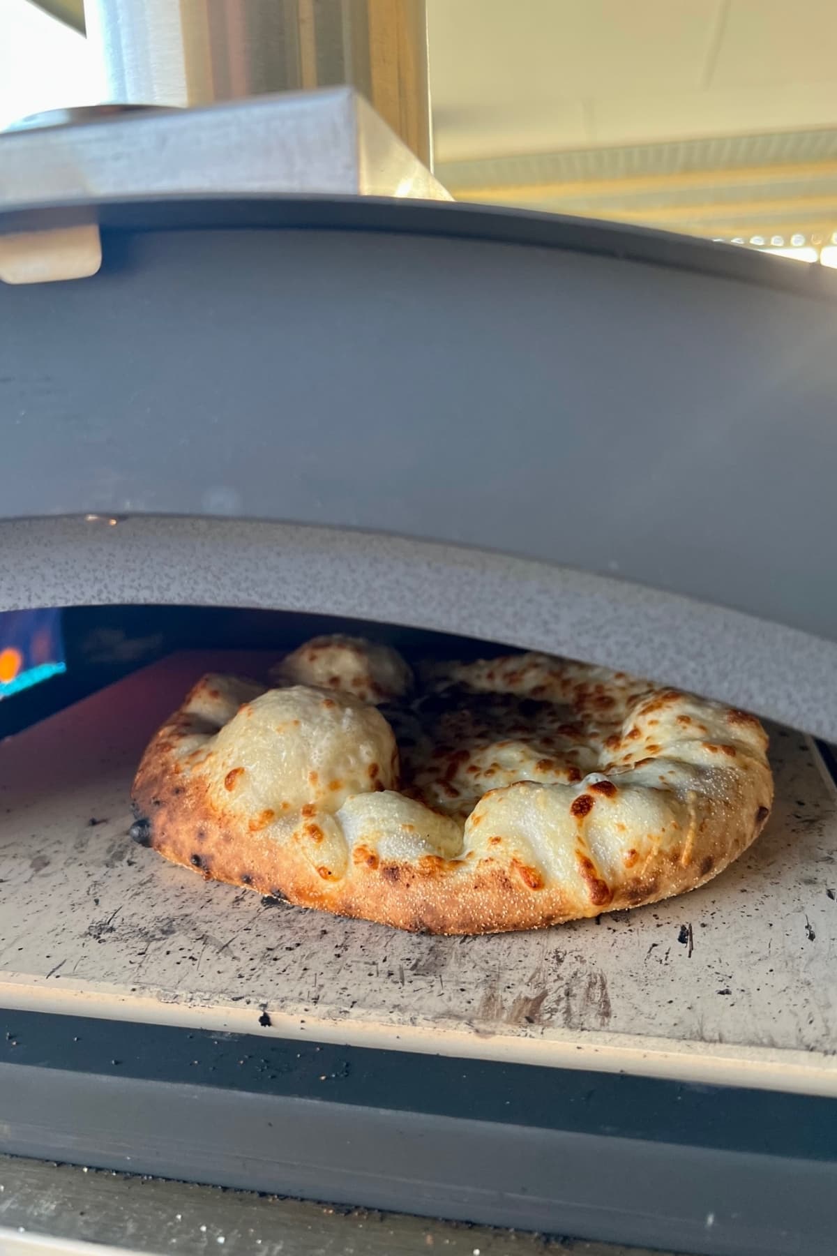 Sourdough discard pizza crust with huge bubbles being baked on a pizza stone inside a gas pizza oven.