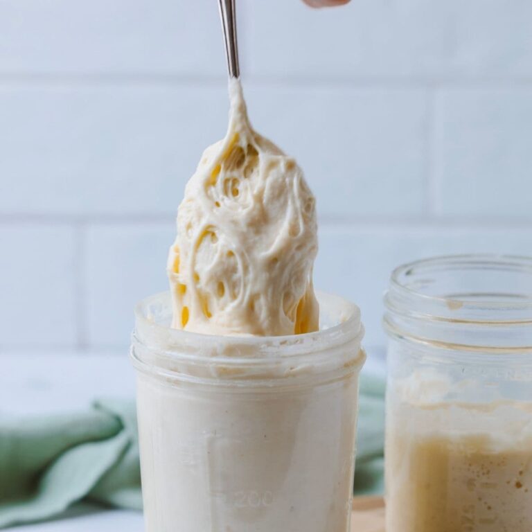 A jar of sourdough starter with a spoon pulling all the bubbly mixture from the top of the jar.