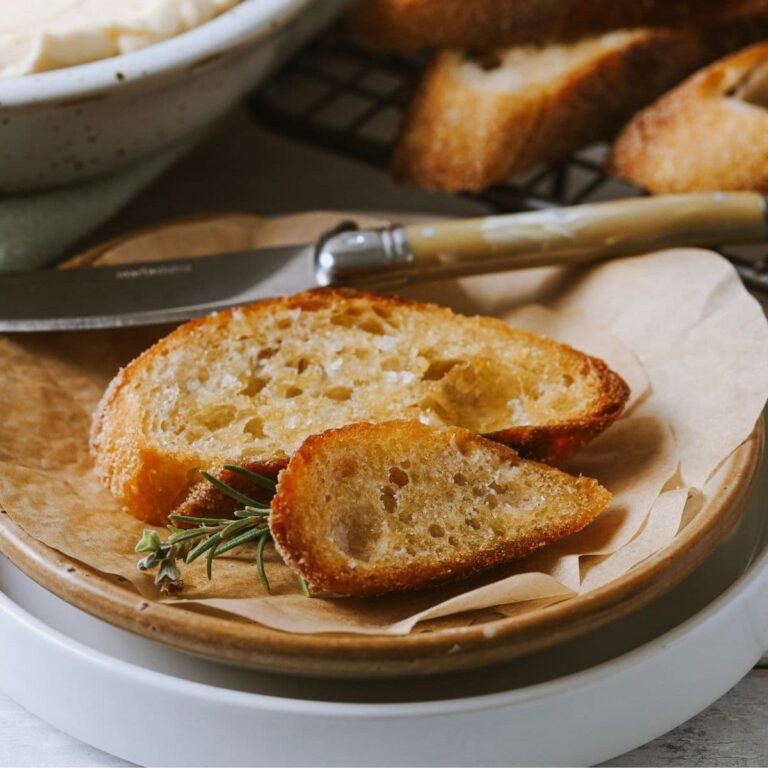 A close up photo of sourdough crostini on a plate with a small spreader.