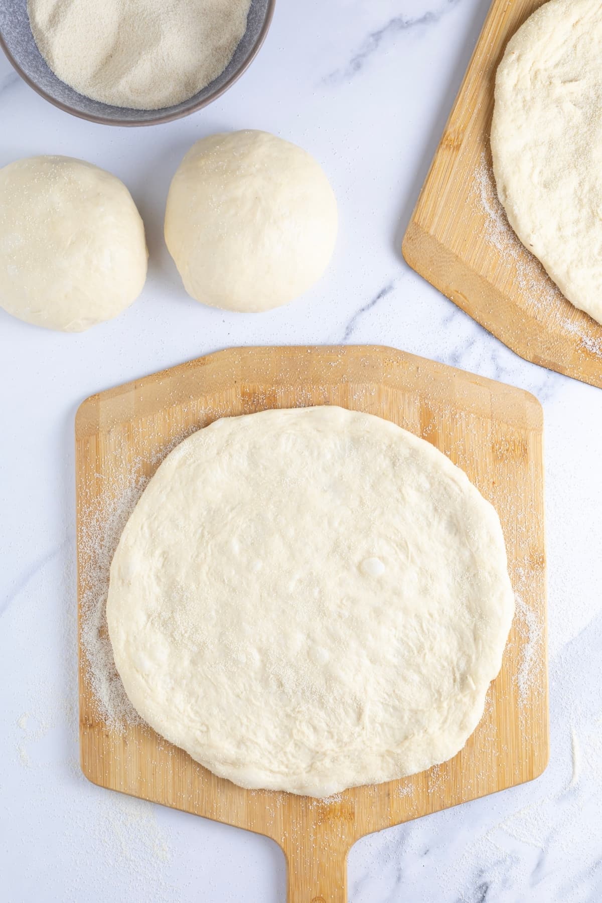 Sourdough discard pizza dough that has been pushed out into a round pizza and laid on a wooden pizza peel. You can also see two other dough balls next to the pizza peel.