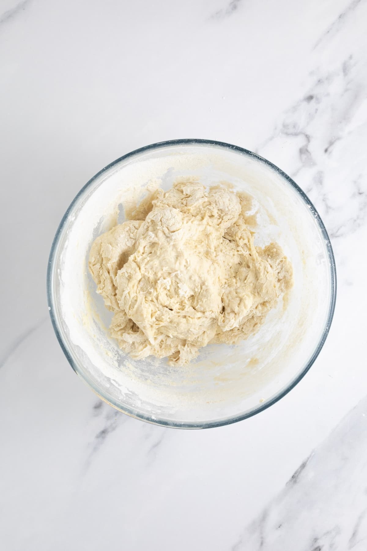 A glass bowl filled with a rough, dry sourdough discard pizza dough that has only just been brought together.