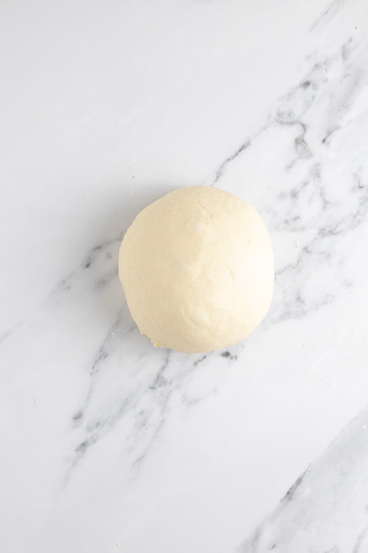 A soft, supple ball of sourdough discard pizza dough that has been kneaded into a smooth ball.