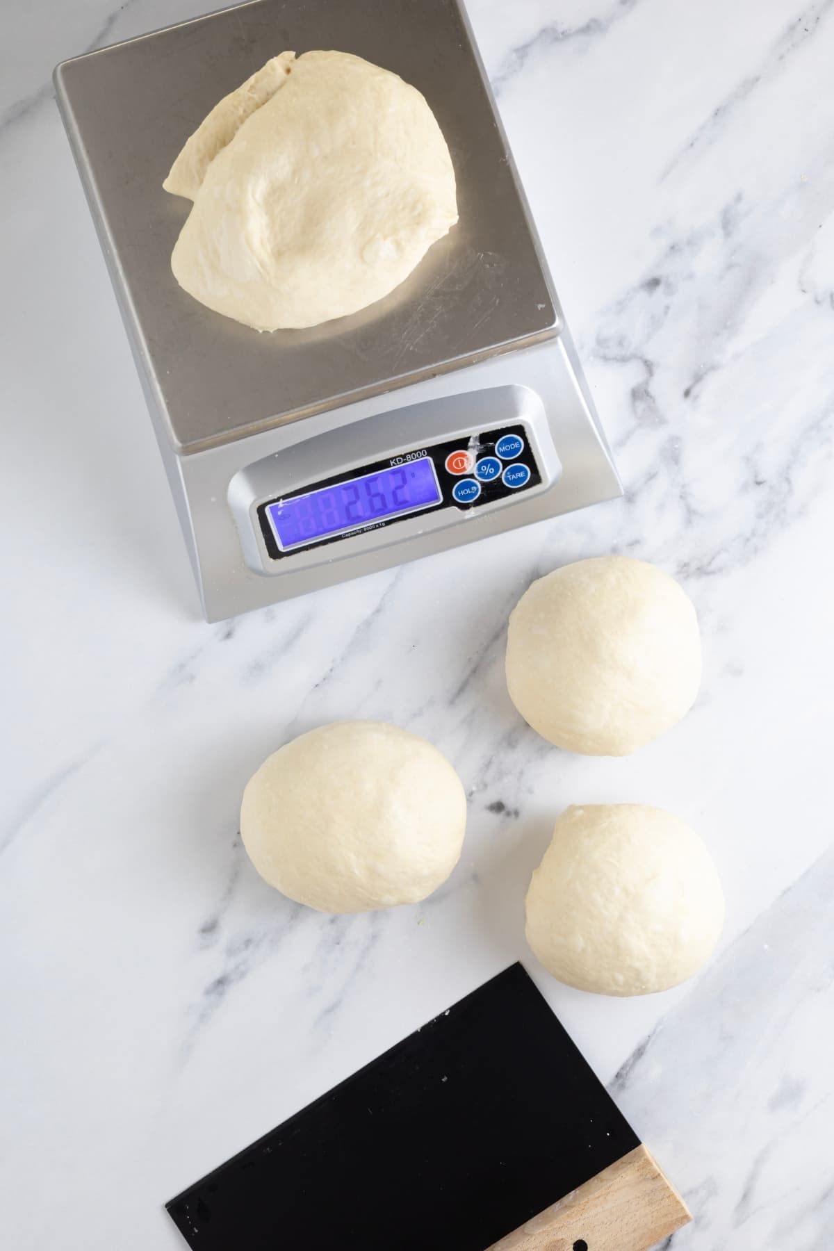 Sourdough discard pizza dough that has been cut into balls and is being weighed on a digital kitchen scale.