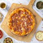 A sourdough discard pizza made with sourdough discard pizza dough that has been topped with pepperoni and mozzarella. The pizza is uncut and displayed on a wooden pizza peel.