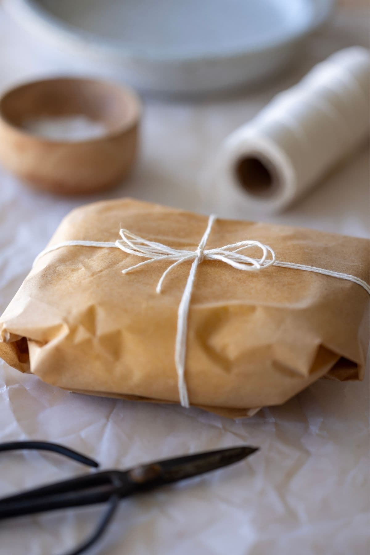 A batch of homemade butter that has been wrapped in parchment paper and tied with string.