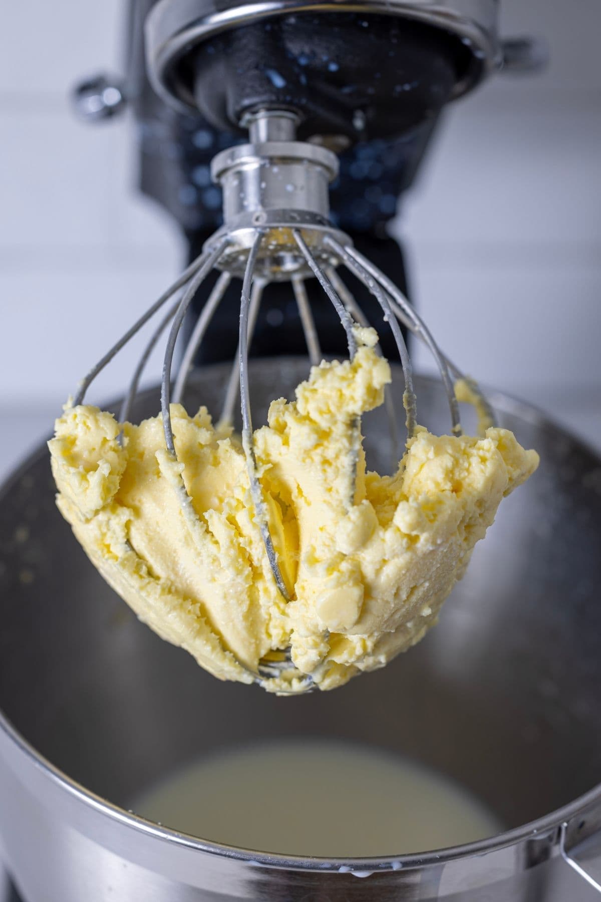 A close up photo of the whisk attachment of the KitchenAid with the yellow cultured butter in the whisk and the cloudy buttermilk in the bowl underneath.