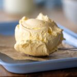 A large scoop of cultured butter sitting on a vintage spoon. There is a little flaky sea salt sprinkled on top.