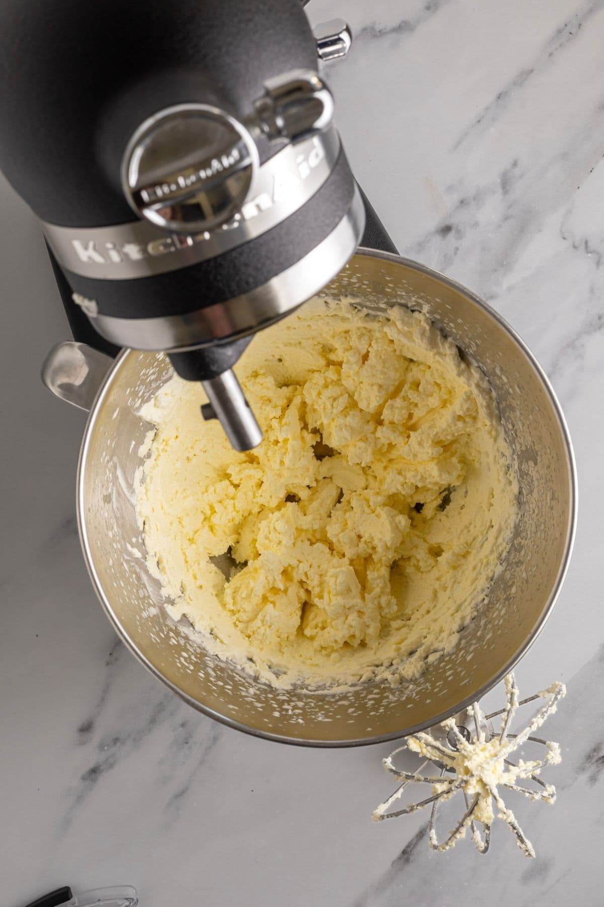 Grainy cream shown in the bowl of a stand mixer right before it splits into butter.
