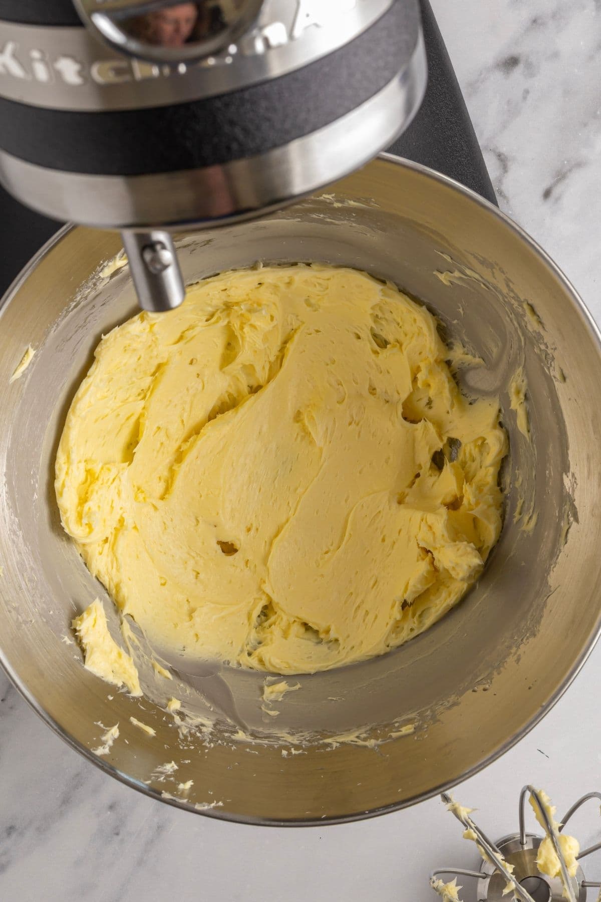 A photo taken from above to show a batch of homemade butter that has just been whipped with salt in the bowl of a stand mixer.