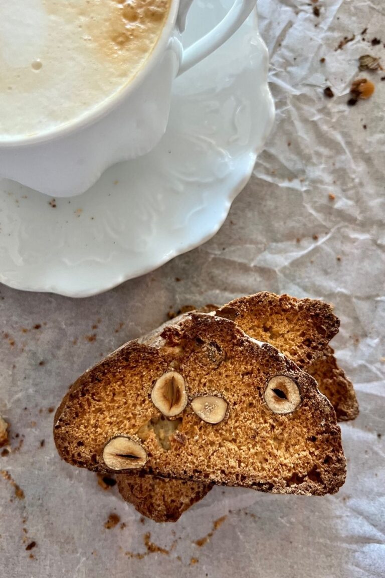 Sourdough biscotti stacked on a white background. There is a coffee cup displayed in the top left of the photo.