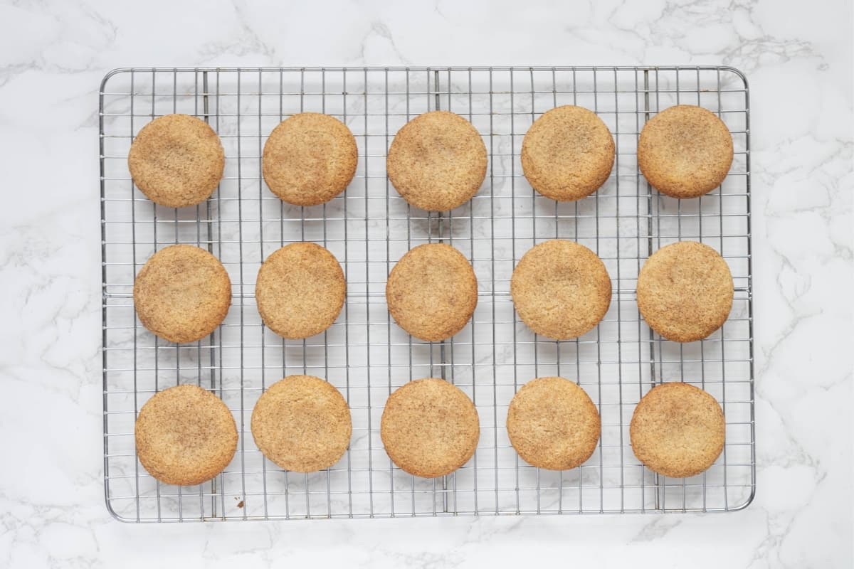 A batch of sourdough snickerdoodle cookies cooling on a wire rack.