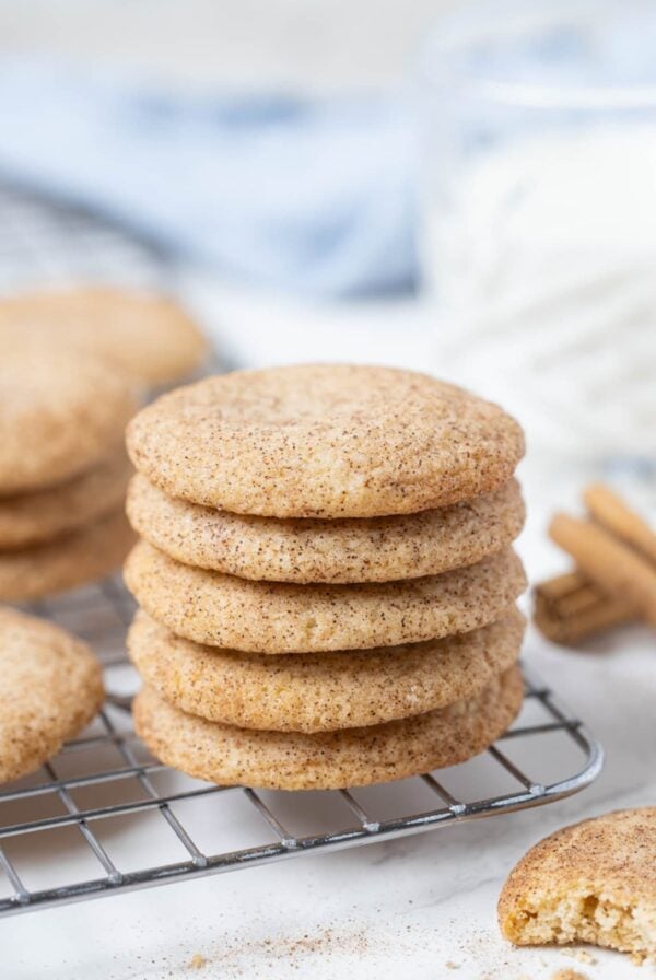 A stack of sourdough snickerdoodle cookies sitting on a wire baking rack. There is a pale blue linen napkin in the background.