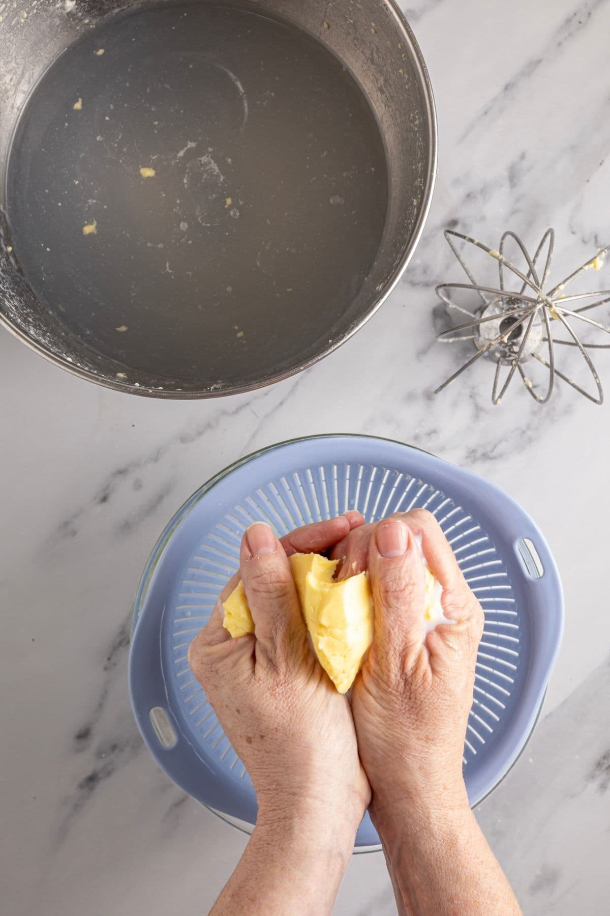 A photo showing buttermilk being squeezed out of a batch of homemade butter over a plastic blue strainer.