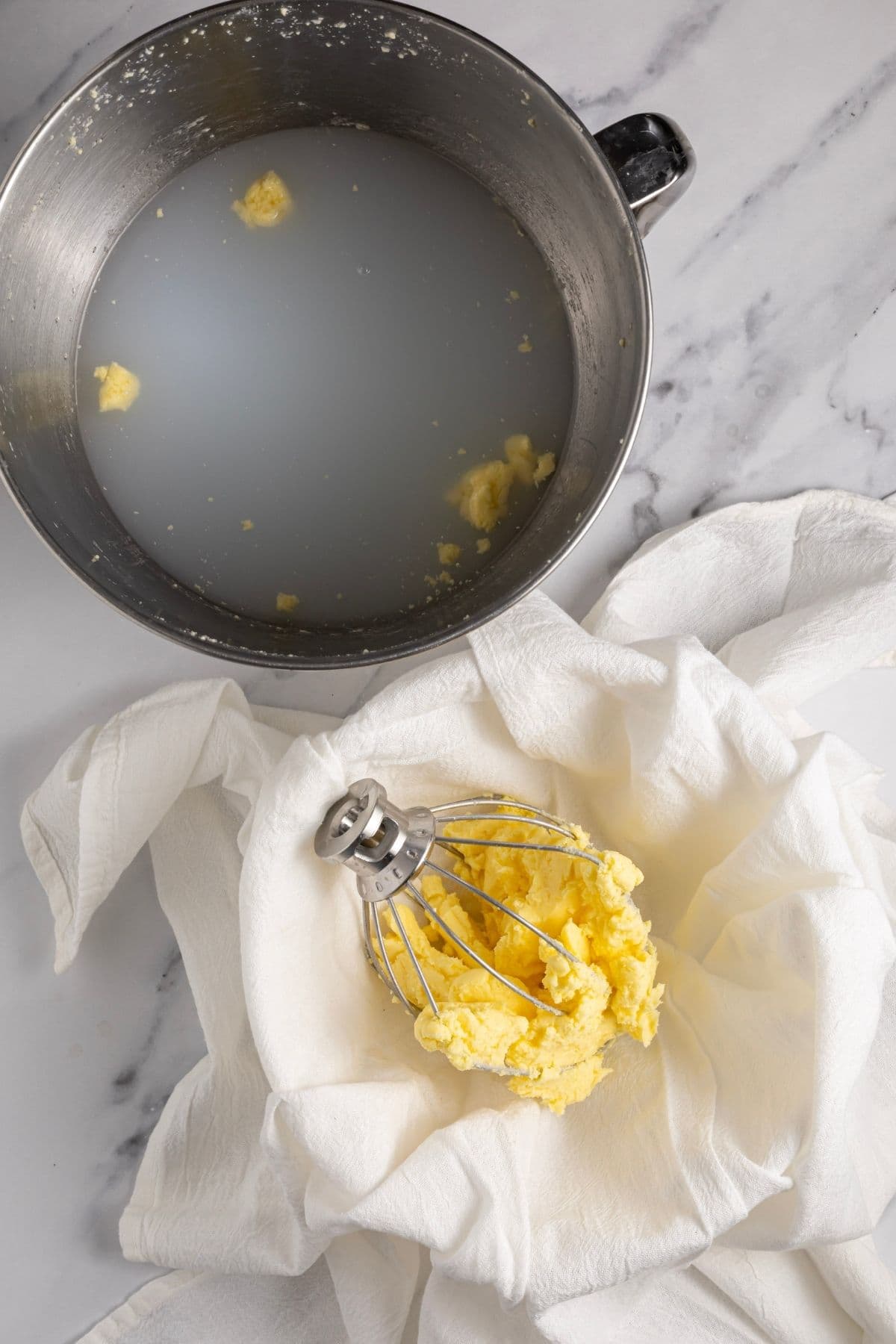 A top down photo showing the cloudy water in a KitchenAid bowl used to wash butter. The butter is sitting in a cloth lined bowl next to the KitchenAid bowl.