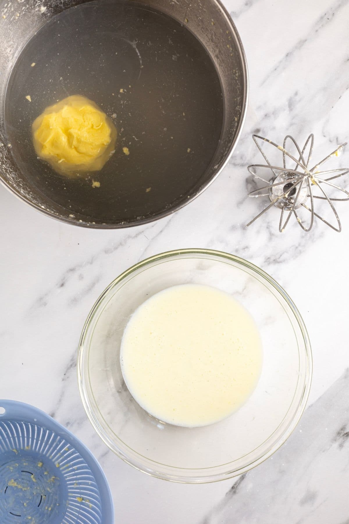 A photo showing a glass bowl of buttermilk that has just been strained from a batch of fresh butter. The butter itself is floating in a stainless steel bowl of cold water ready to be washed.