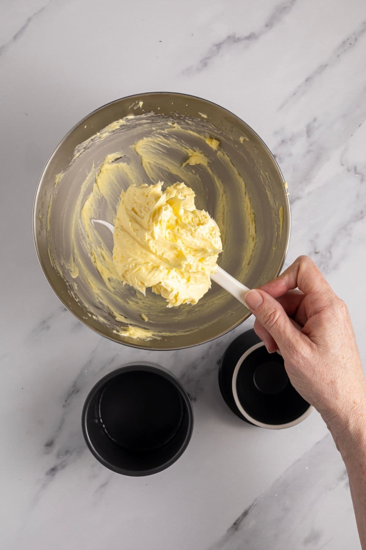 Whipped cultured butter being held on a white spatula above a stainless steel bowl. There is a butter bell underneath ready to hold the freshly whipped butter.
