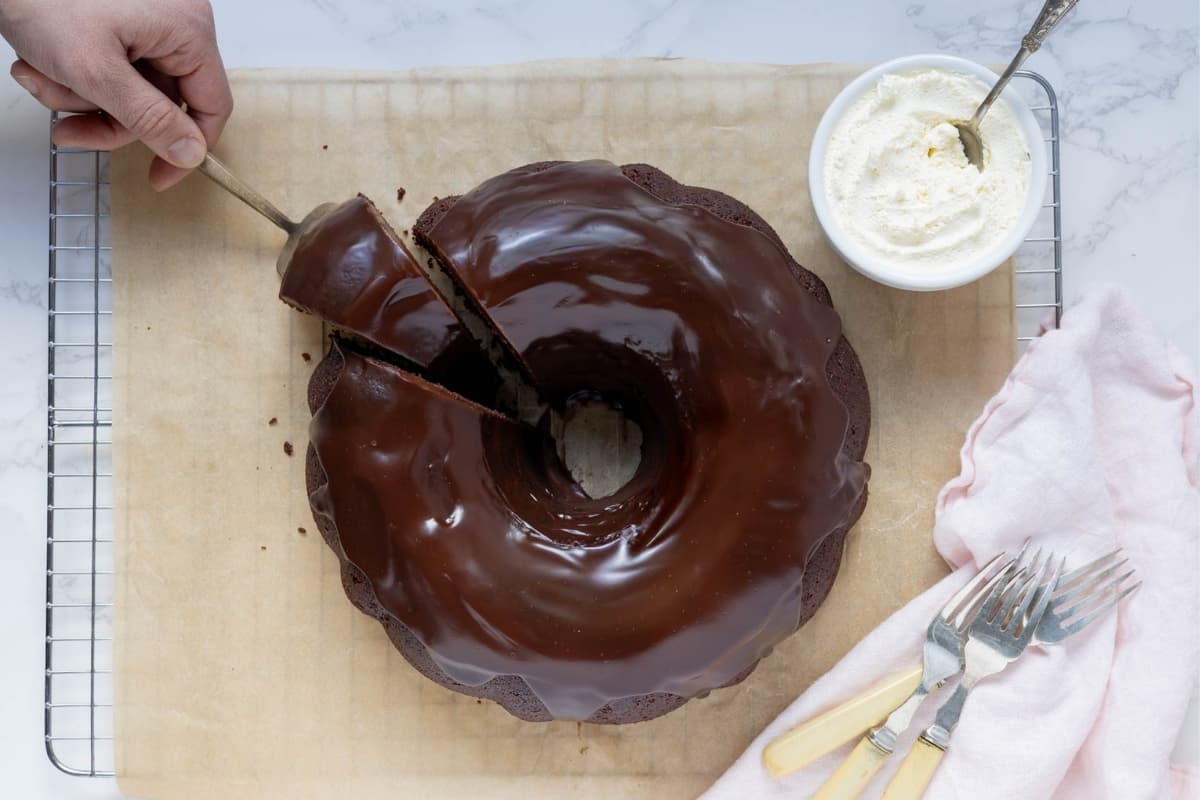 Cake server lifting a slice of sourdough chocolate cake coated in rich chocolate ganache.