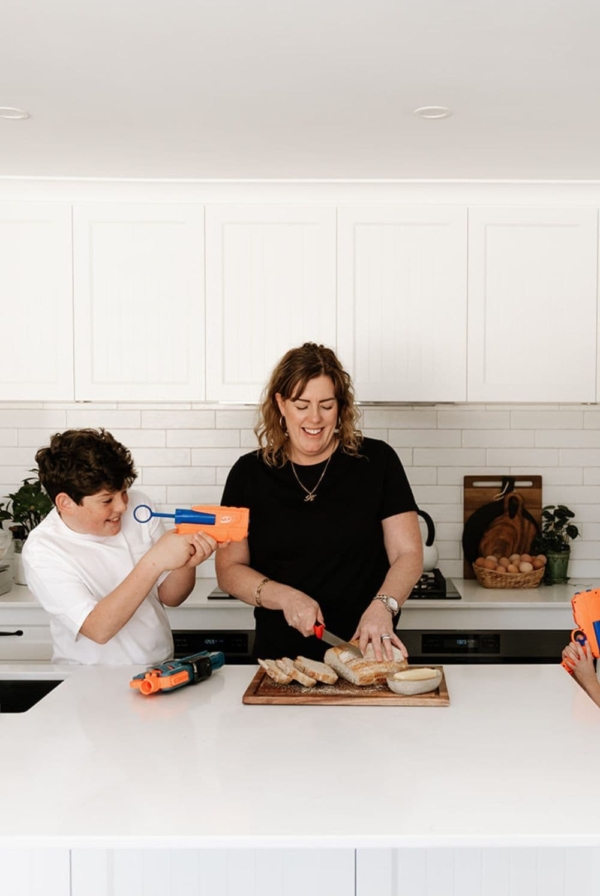 Sourdough for busy moms - easy sourdough recipe for time poor moms - this photo shows a mom and son slicing sourdough bread while there is a Nerf blaster battle going on around them.