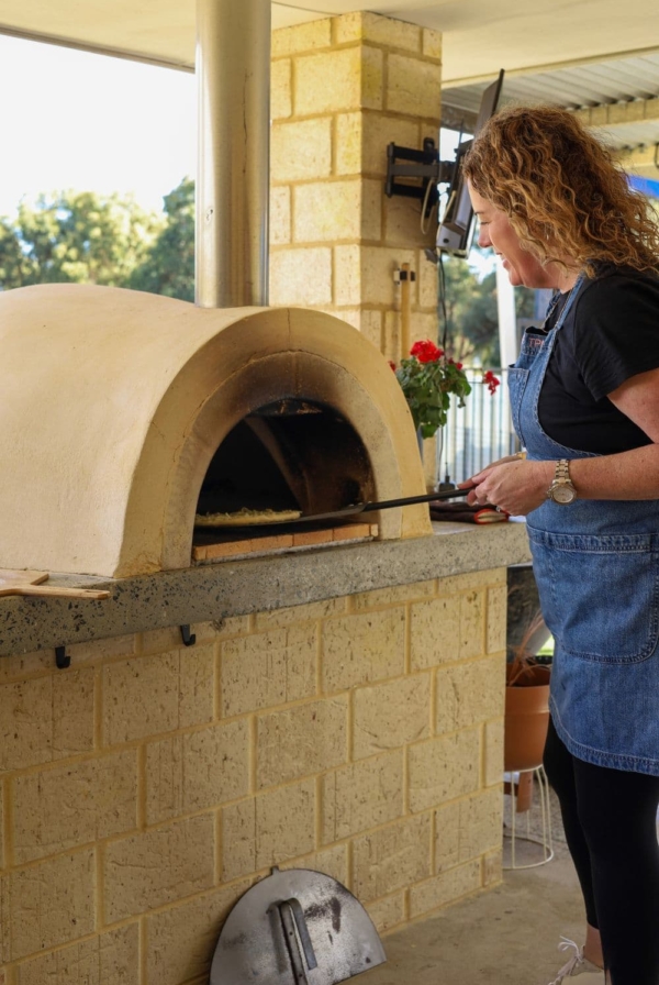 Kate from The Pantry Mama cooking a pizza using a wood fired pizza oven.
