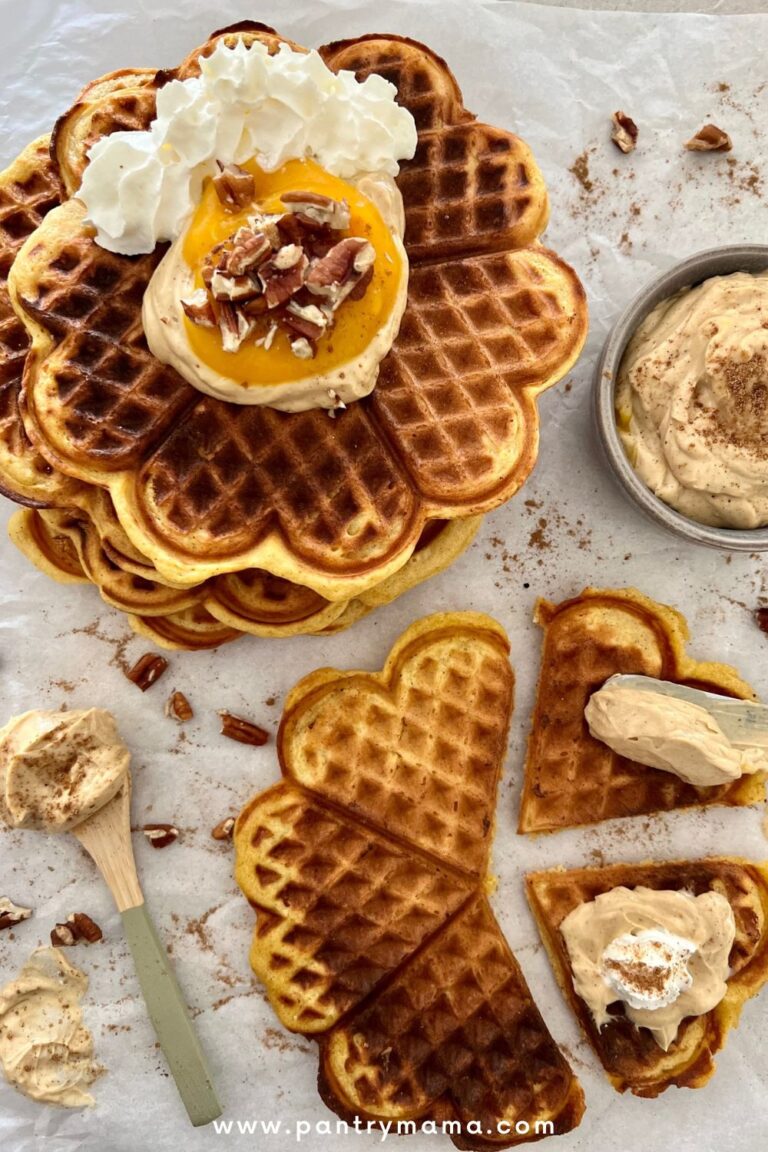 Sourdough Pumpkin Waffles made in a round waffle maker. There is a stack of waffles in the top left corner topped with whipped cream and pecans.