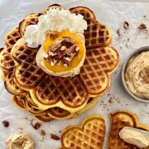 A photo showing a stack of sourdough pumpkin waffles topped with cream cheese and walnuts.