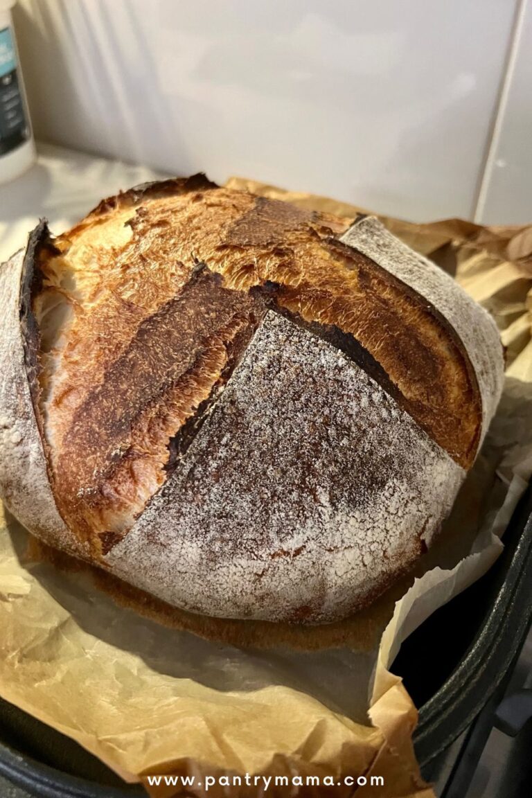 long fermented sourdough bread fresh out of the oven and sitting on a piece of parchment paper on a cast iron Dutch Oven base