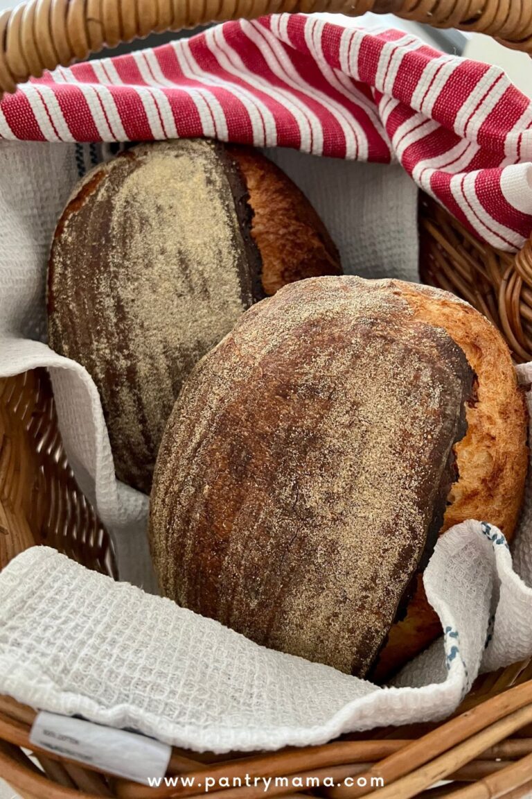 TWO LOAVES OF SAME DAY SOURDOUGH BREAD NESTLED IN A CANE BASKET WITH A RED AND WHITE DISH TOWEL