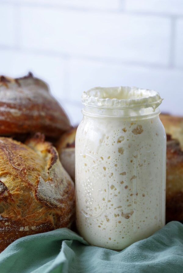 A jar of sourdough starter sitting next to a pile of freshly baked sourdough bread.