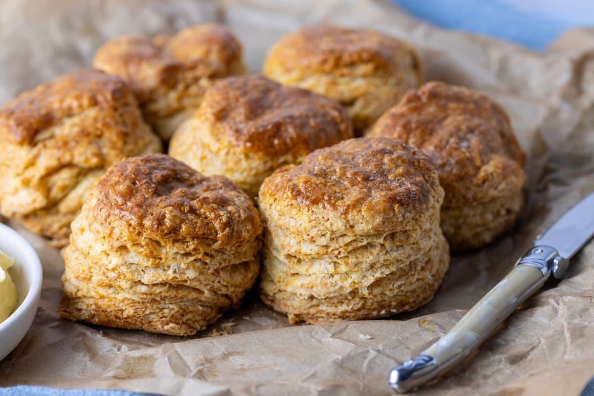 A horizontal image of flaky sourdough biscuits that have been taken out of the pan they're baked in and sat on a piece of parchment paper. You can see the flaky layers in the front two biscuits.