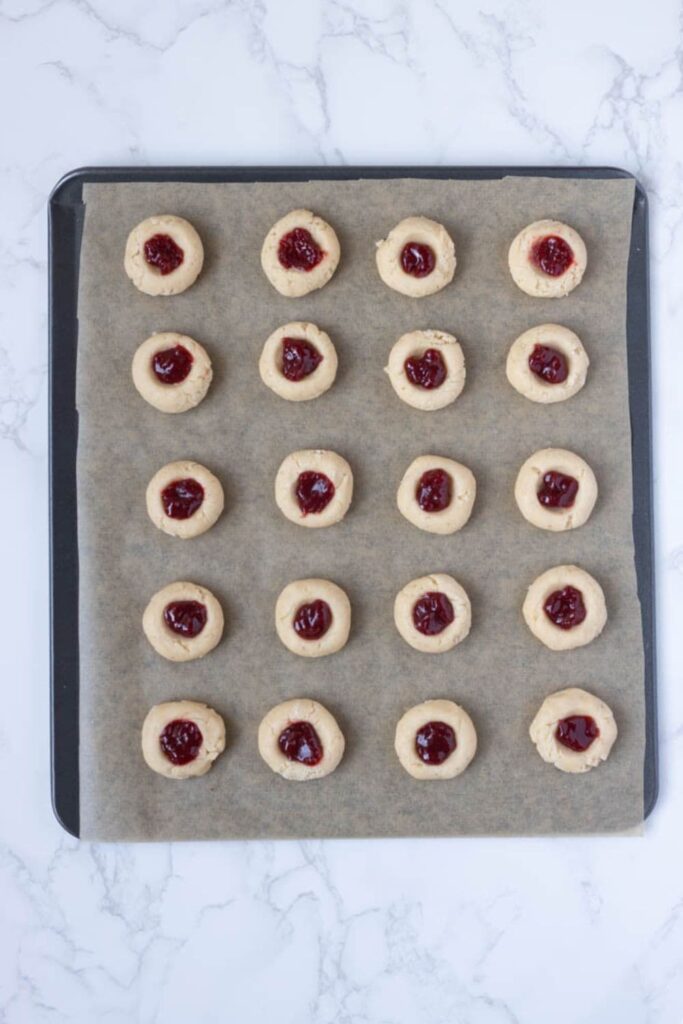 A parchment lined tray with sourdough discard thumbprint cookies filled with strawberry jam.