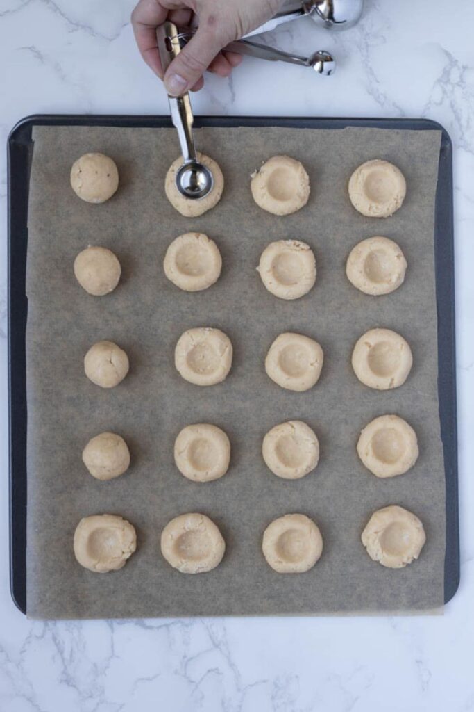 A tray of sourdough discard thumbprint cookies that have had an indent made in them with a small spoon.