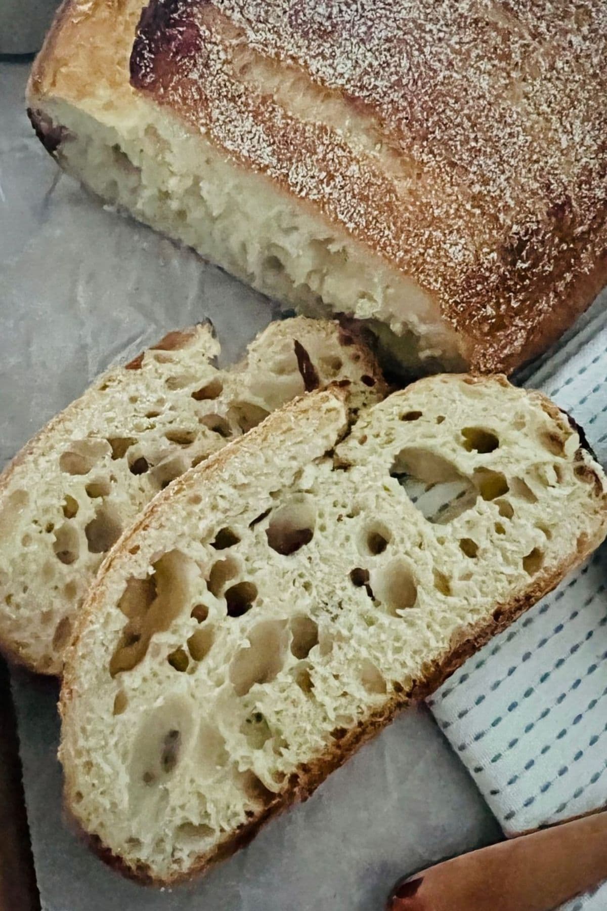 A loaf of sourdough bread that has been sliced. There are two slices laying face up so you can see the very uneven crumb and large tunnels caused by under-fermentation.