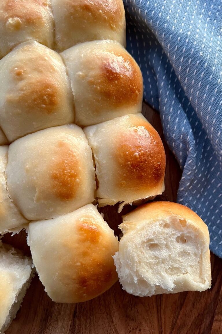 Soft Sourdough Dinner Rolls sitting on a wooden board. There is a blue dish towel sitting to the right.