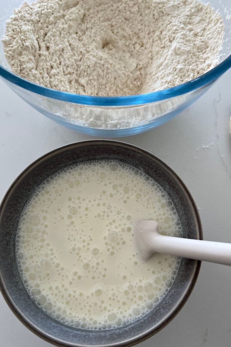 How to convert yeast recipe to sourdough - small blue bowl with bubbly sourdough starter and a white jar spatula. There is a glass bowl of flour in the background.