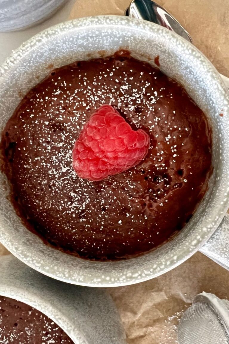 Sourdough discard mug cake served in a stoneware mug. The photo is taken above the mug so you can see the top of the mug cake with a fresh red raspberry on top.