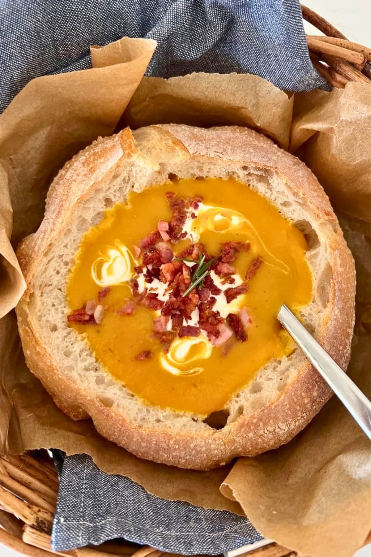 A sourdough bread bowl filled with bright orange pumpkin soup topped with sour cream, bacon pieces and parsley.