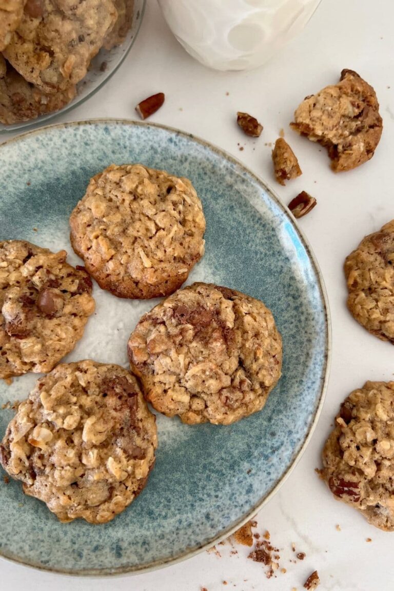 4 sourdough discard cowboy cookies on a blue stoneware plate. There is a glass of milk in the background and some cookie crumbs around the edges of the plate.