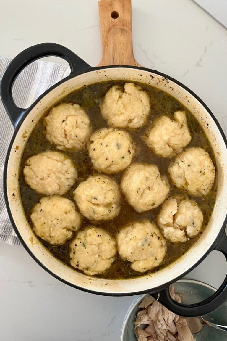 Black enamel Dutch Oven full of chicken soup with 12 sourdough dumplings floating on the top.