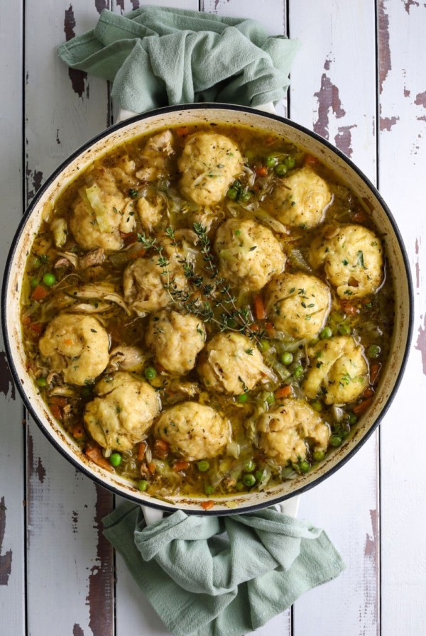 A large, round pan of sourdough chicken and dumplings full of vegetables and topped with fresh thyme sprigs.