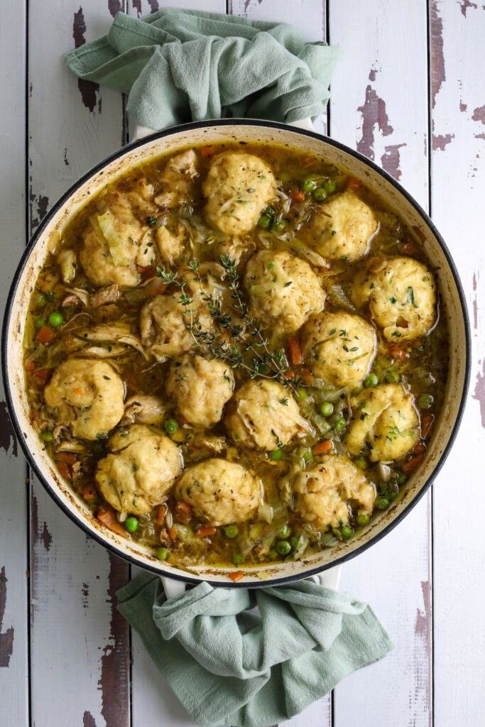 A large, round pan of sourdough chicken and dumplings full of vegetables and topped with fresh thyme sprigs.