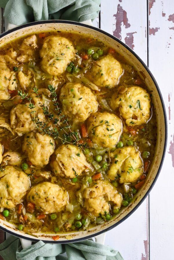 A large, round pan of sourdough chicken and dumplings full of vegetables and topped with fresh thyme sprigs.